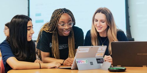 Three students work around a laptop, smiling