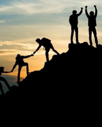 people in silhouette climb a mountain, helping eachother up and celebrating at the top