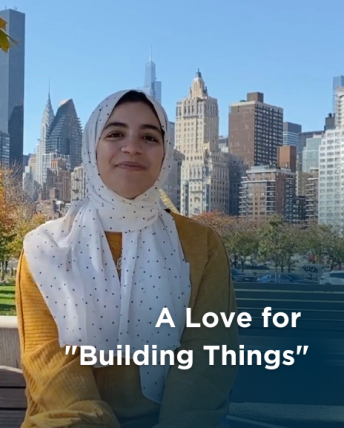 A woman in a yellow shirt and white hijab smiles in front of the New York City skyline