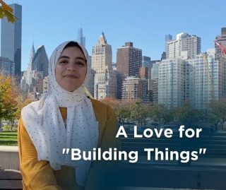 A woman in a yellow shirt and white hijab smiles in front of the New York City skyline