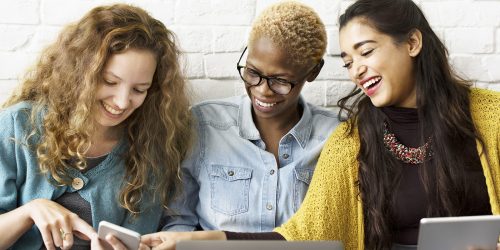 Three women looking at a laptop and cellphone