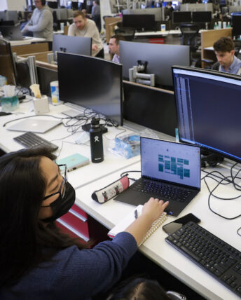 A Break Through Tech Chicago Sprintern works at a laptop connected to larger monitor displays at the financial services firm PEAK6